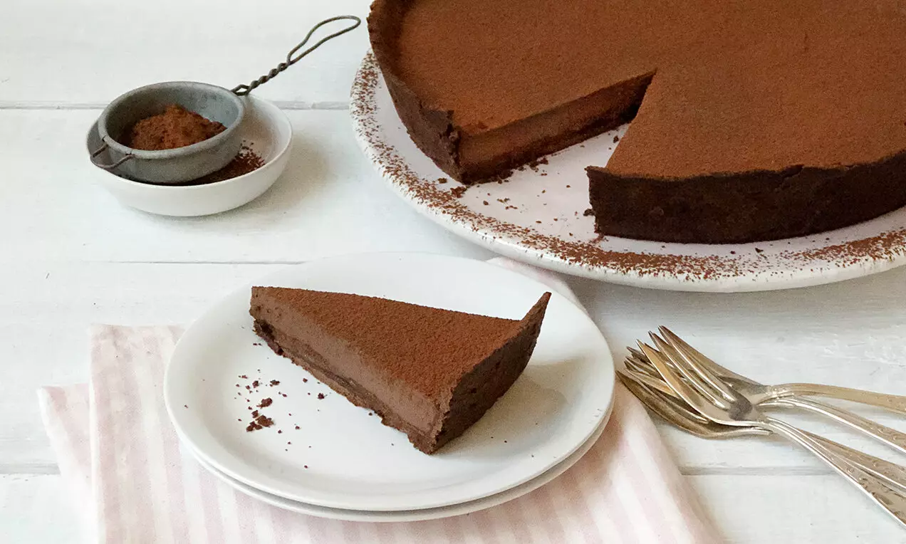 Tartă vegană de ciocolată cu o cremă densă maro închis, blat fin și topping pudrat subtil de cacao pe farfurii albe elegante