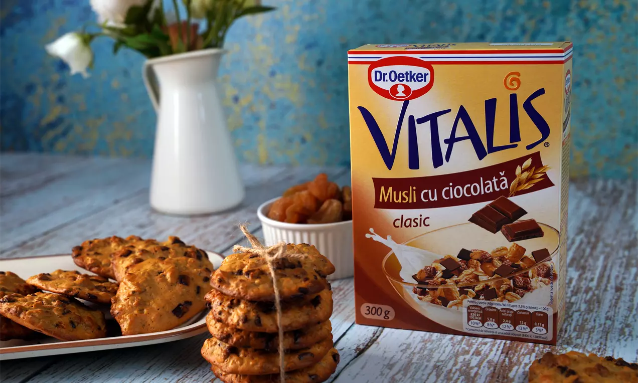 Prăjiturele aurii și crocante cu ghimbir, rotunde, stivuite sau așezate pe o farfurie albă, lângă un bol cu fructe uscate și decor floral