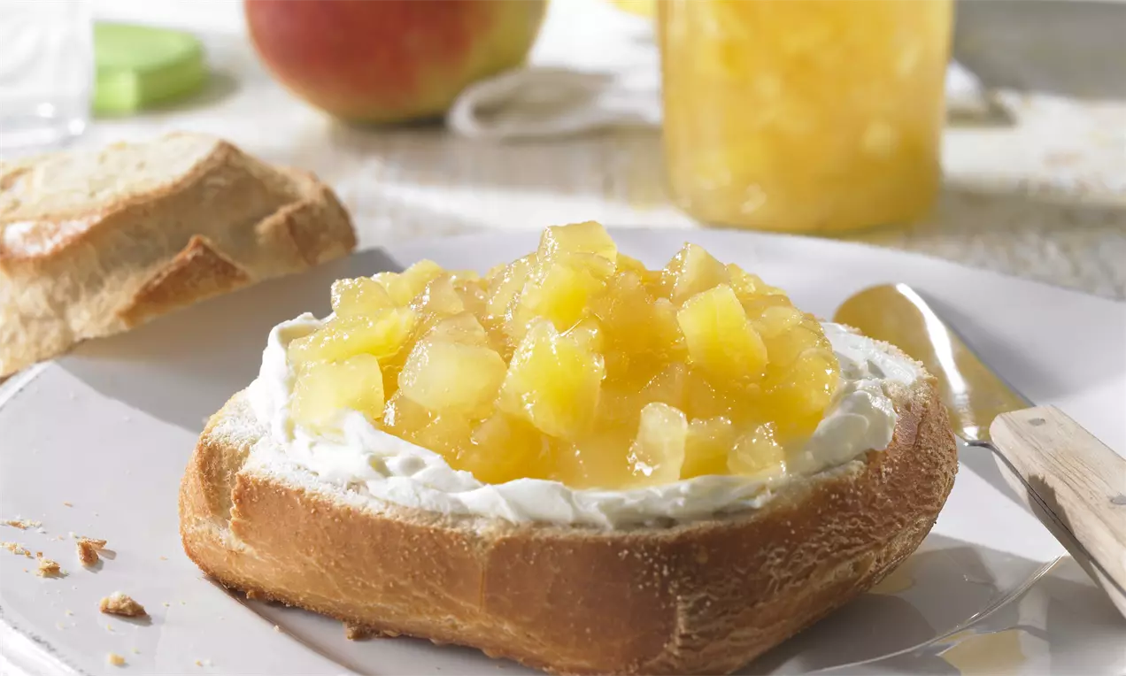 Povestează despre dulceață galben-aurie de mere și ananas cu bucăți translucide, întinsă peste frișcă pe o felie de pâine prăjită