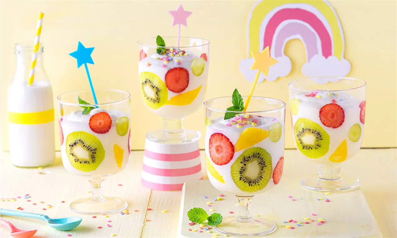 Desert cremă paradis cu strat alb pufos, felii vibrante de kiwi, căpșuni și banane, decorat cu steluțe colorate și frunze de mentă