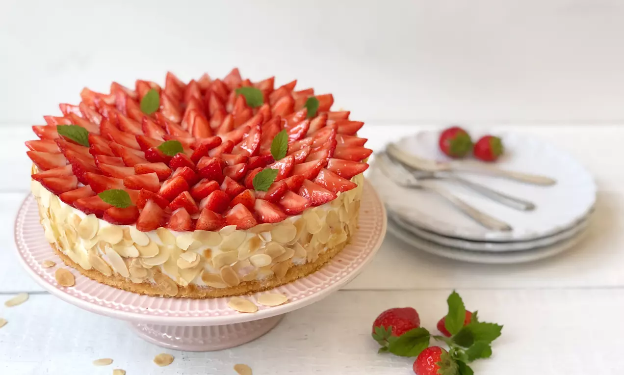 Tort cu brânză pe blat auriu, decorat cu felii strălucitoare de căpșuni și frunze de mentă, așezat pe un platou roz pal