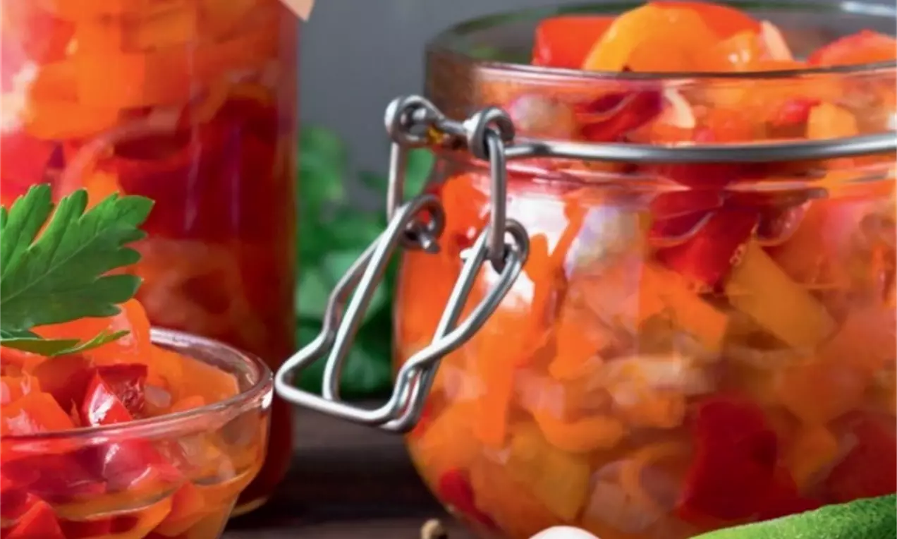 Salată de vară viu colorată, cu bucăți de ardei roșu și galben într-un borcan de sticlă transparentă, alături de castraveți și verdeață