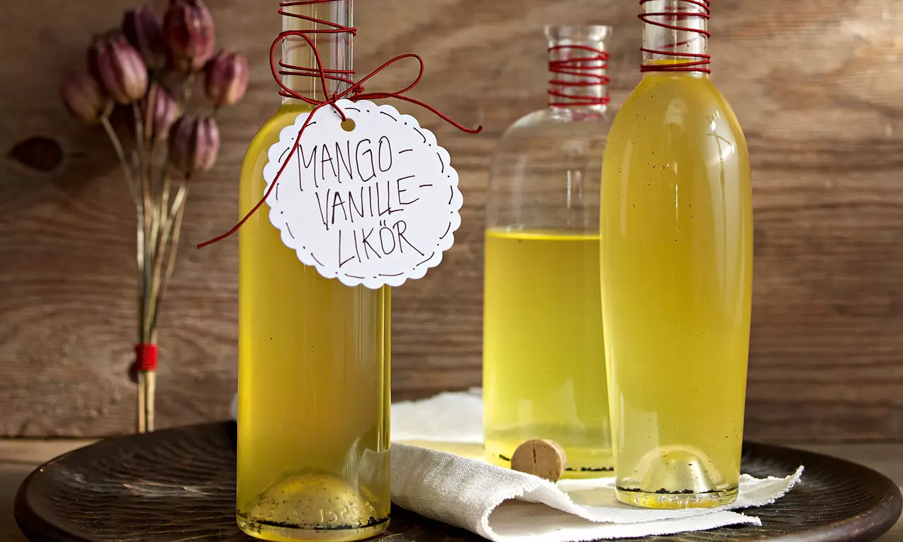 Sticle elegante din sticlă transparentă cu lichior galben intens de mango și vanilie, decorate cu șnur roșu și etichetă manuală albă