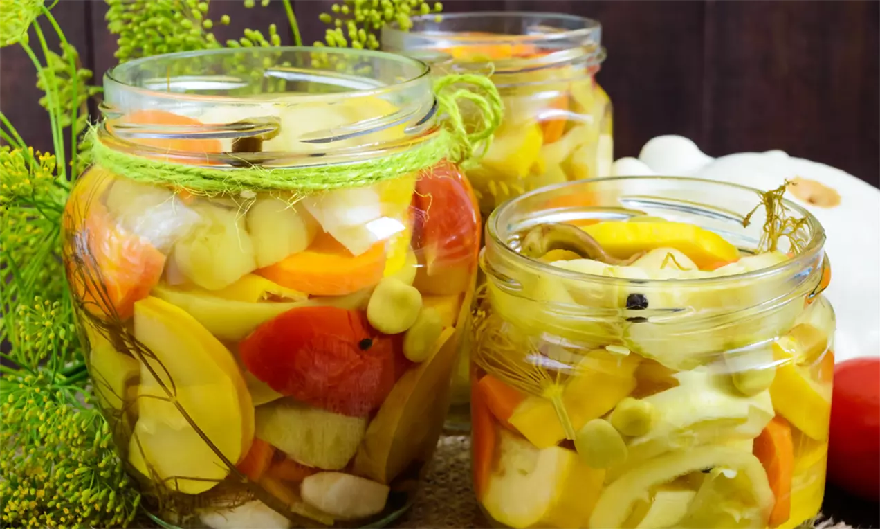 Borcan cu salată mixtă de ardei, felii colorate de galben, portocaliu și roșu alături de rondele de castraveți în saramură, decorat cu fire de mărar