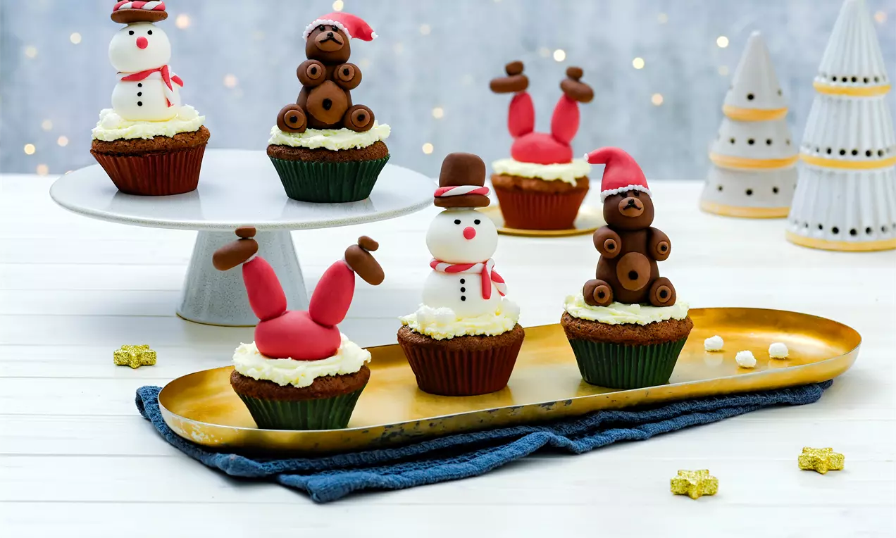 Brioșe aurii decorate cu figurine din fondant colorat, în formă de oameni de zăpadă, reni și pălării de Moș Crăciun, așezate pe un platou elegant
