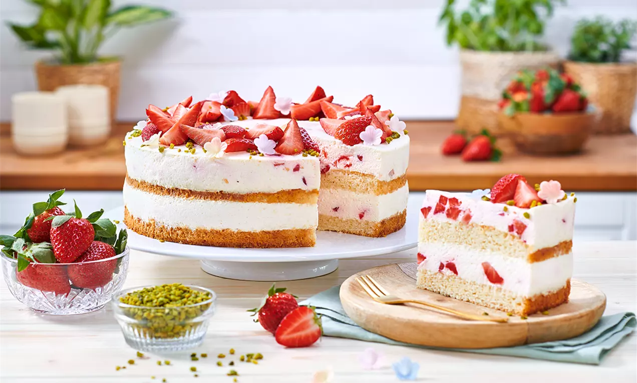 Tort vegan stratificat cu blat auriu pufos, cremă albă fină, căpșuni proaspete și decor de flori mici pe un platou alb elegant